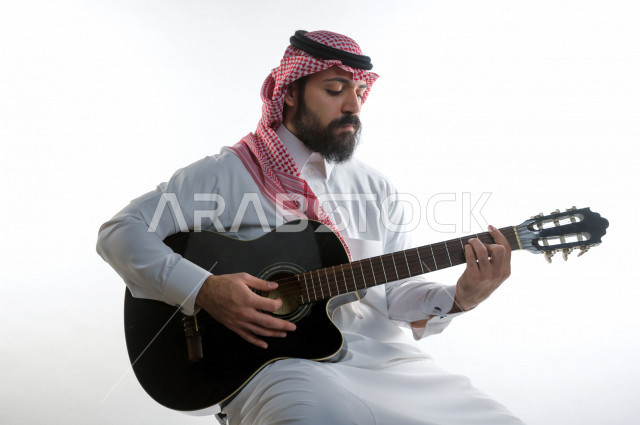 بورتريه شاب سعودي عربي خليجي يعزف على  الجيتار( آلة وترية) ، شاب باللباس السعودية التقليديه بخلفية بيضاء ، آلة موسيقية ، مجال صوتي و فني