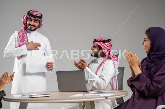 تحقيق أهداف واستراتيجيات الشركة، مفهوم التركيز والدقة في الإنجاز، إيماءات الفرح والسرور، الحوارات والنقاشات ضمن فريق العمل، بورتريه لموظفين عربيين خليجيين سعوديين يقومون بالتصفيق وتهنئة زميلهم, ورشات عمل وتدريب، خلفية رمادية