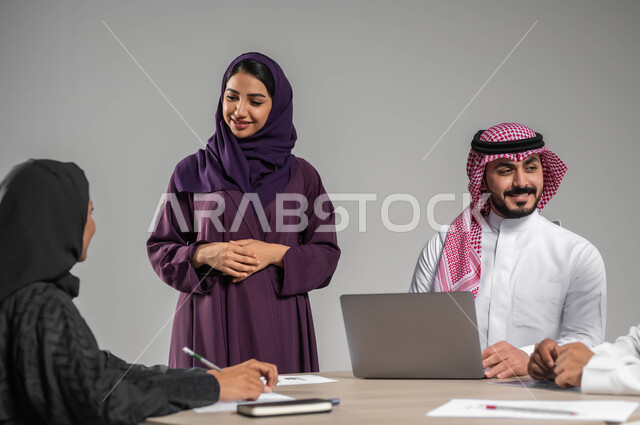Providing a comfortable work environment, workshops and training, discussions and dialogues between colleagues, Saudi professions and jobs, a portrait of a Saudi-Gulf Arab work team cooperating to achieve the company’s strategies and goals, using modern techniques and technology, a gray background