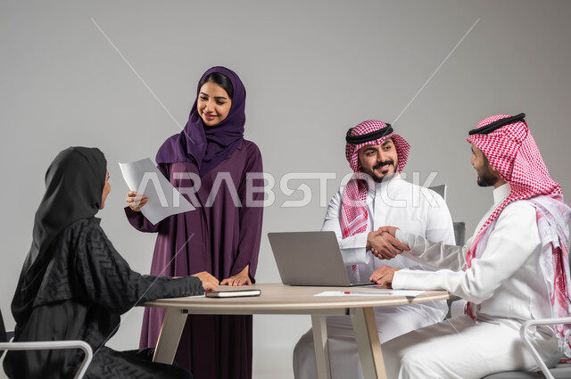 اتفاقيات وحوارات ضمن الفريق، مهن ووظائف سعودية، توفير بيئة عمل مريحة، بورتريه لموظفة عربية سعودية خليجية مبتسمة تحمل بيدها الأوراق تتناقش مع زملائها بإيماءات السرور، إستخدام التقنيات والتكنولوجيا الحديثة، خلفية رمادية