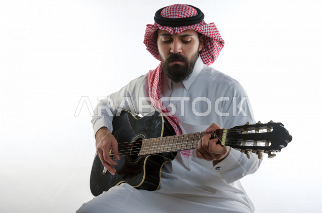 بورتريه شاب سعودي عربي خليجي يعزف على  الجيتار( آلة وترية) ، شاب باللباس السعودية التقليديه بخلفية بيضاء ، آلة موسيقية ، مجال صوتي و فني