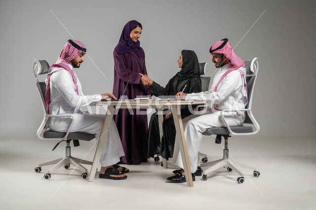 Handshake and agreement in completing work, professionalism and dedication to business development, exchange of successful experiences and information, cooperation and understanding between the team, expressions of deep friendship, portrait of Saudi Gulf Arab colleagues in a meeting, wearing traditional Saudi dress, gray background