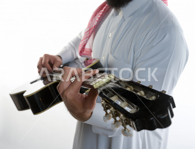 بورتريه شاب سعودي عربي خليجي يعزف على  الجيتار( آلة وترية) ، شاب باللباس السعودية التقليديه بخلفية بيضاء ، آلة موسيقية ، مجال صوتي و فني