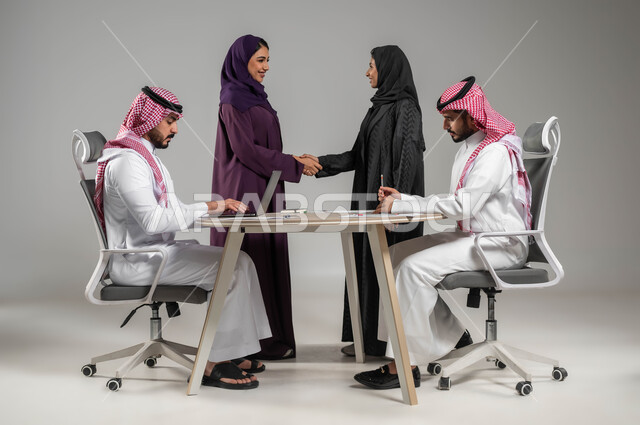 المصافحة والاتفاق في تطوير الاعمال, تبادل الخبرات والمعلومات الناجحة, التعاون والتفاهم بين الفريق, تعابير الصداقة العميقة, بورتريه لزملاء عرب سعوديين خليجيين في اجتماع, ارتداء اللباس السعودي التقليدي, بيئة العمل المريحة في الشركة السعودية, خلفية رمادية