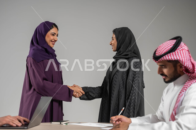 التعاون والتفاهم بين الفريق, تبادل الخبرات والاتفاقيات الناجحة, تعابير الصداقة العميقة, بورتريه لزملاء عرب سعوديين خليجيين في اجتماع, ارتداء اللباس السعودي التقليدي, بيئة العمل المريحة في الشركة السعودية, خلفية رمادية