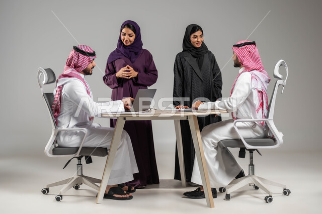 Integrating technology and technology with work, comfortable work environment in a Saudi company, organizing and managing a work concept schedule, portrait of Saudi Gulf Arab employees in a meeting, wearing traditional Saudi dress, gaining experience and expanding the network of professional relationships, gray background