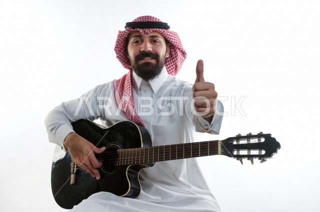 بورتريه شاب سعودي عربي خليجي يعزف على  الجيتار( آلة وترية) ، شاب باللباس السعودية التقليديه بخلفية بيضاء ، آلة موسيقية ، مجال صوتي و فني