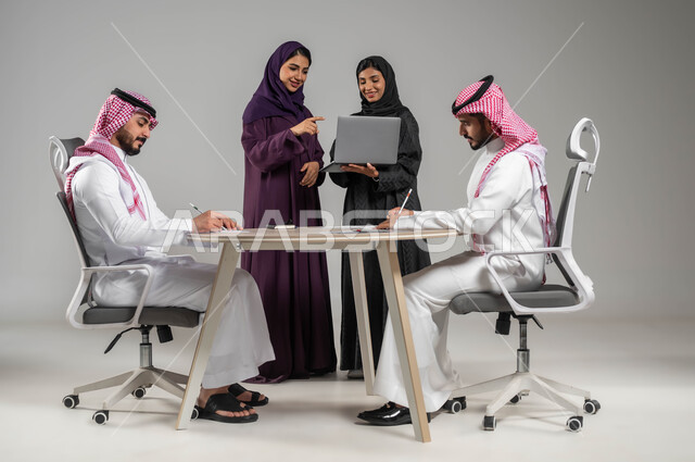 الإشارة الى اللابتوب بهدف توضيح العمليات, مفهوم الشراكة والتعاون, توفير بيئة عمل مناسبة, بورتريه مقرب لزملاء عرب سعوديين خليجيين في اجتماع, ارتداء اللباس السعودي التقليدي, استخدام التقنيات الحديثة في تطوير الاعمال, خلفية رمادية