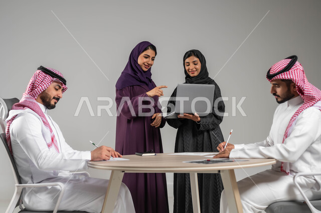 مفهوم الشراكة والتعاون, توجيه الجهود لتحقيق أهداف الشركة, الإشارة الى الحاسوب المحمول بهدف توضيح العمليات, بورتريه مقرب لزملاء عرب سعوديين خليجيين في اجتماع, ارتداء اللباس السعودي التقليدي, خلفية رمادية