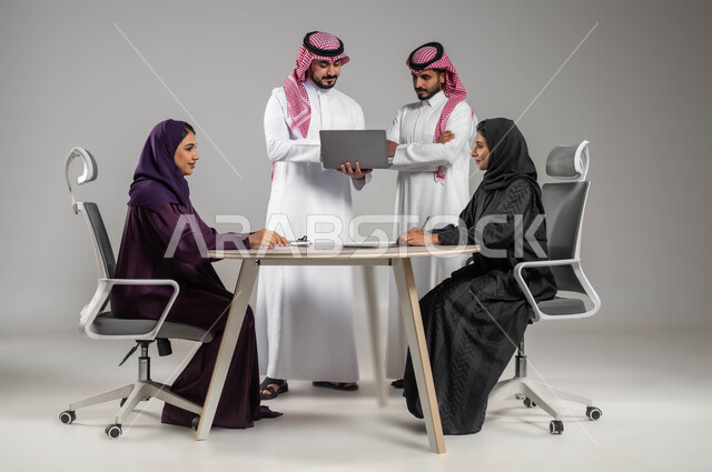The desire to develop professional work, provide a suitable work environment, use modern devices and methods to explain work, portrait of Saudi Gulf Arab employees in a meeting, wearing traditional Saudi dress, gray background