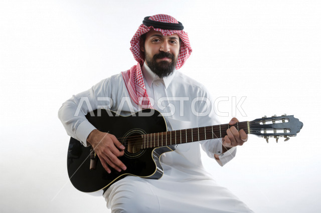 بورتريه شاب سعودي عربي خليجي يعزف على  الجيتار( آلة وترية) ، شاب باللباس السعودية التقليديه بخلفية بيضاء ، آلة موسيقية ، مجال صوتي و فني