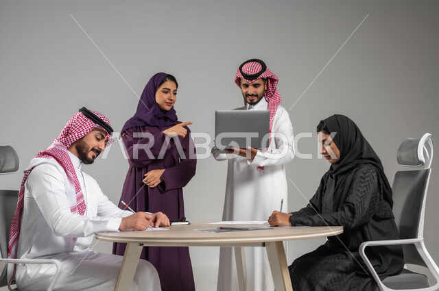 استخدام الاجهزة والتقنيات الحديثة في تطوير الاعمال, الاشارة الى الحاسوب المحمول بهدف توضيح العمليات, توفير بيئة عمل مناسبة, مفهوم الشراكة والعمل الجماعي, بورتيه لموظفين عرب سعوديين خليجيين في اجتماع, ارتداء اللباس السعودي التقليدي, خلفية رمادية