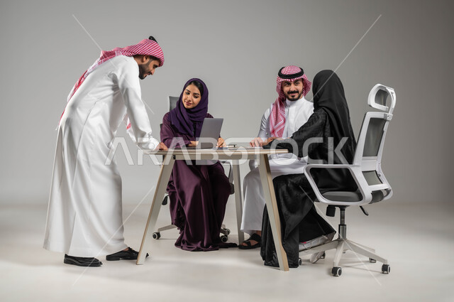 Saudi professions and jobs, discussing next steps, dialogues and discussions within the team, ensuring a clear understanding of the business, focus and hard work, professionalism and dedication to achievement, using the laptop for blogging, portrait of Saudi Gulf Arab employees in a meeting, full-body portrait, gray background
