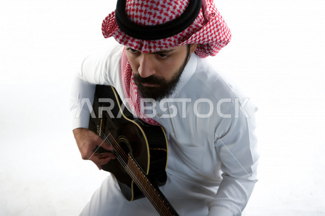 بورتريه شاب سعودي عربي خليجي يعزف على  الجيتار( آلة وترية) ، شاب باللباس السعودية التقليديه بخلفية بيضاء ، آلة موسيقية ، مجال صوتي و فني