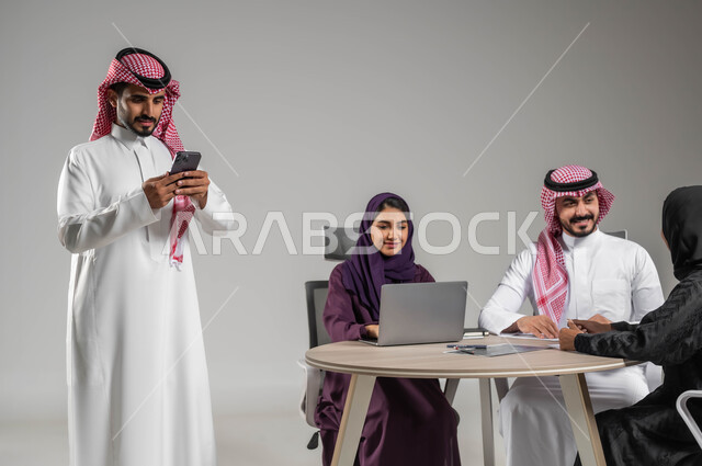 توفير بيئة عمل مناسبة، مهن ووظائف سعودية، الحوارات والنقاشات ضمن الفريق، إنجاز العمل عبر الموبايل، مفهوم الشراكة والتعاون، إستخدام التكنولوجيا الحديثة، الاحترافية والتفاني في العمل، بورتريه لموظفة عربية سعودية خليجية مقوم باجتماع مع زملائها، خلفية رمادية