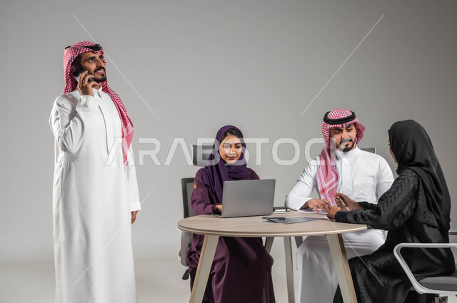 مفهوم الشراكة والتعاون، إستخدام التكنولوجيا الحديثة، إجراء مكالمات عمل، الاحترافية والتفاني في العمل، بورتريه لموظفة عربية سعودية خليجية مقوم باجتماع مع زملائها، مهن ووظائف سعودية، الحوارات والنقاشات ضمن الفريق، توفير بيئة عمل مناسبة، خلفية رمادية