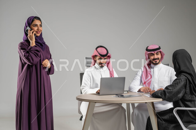 إجراء مكالمات عمل، الاحترافية والتفاني في العمل، إستخدام التكنولوجيا الحديثة ، بورتريه لموظفة عربية سعودية خليجية مقوم باجتماع مع زملائها، مهن ووظائف سعودية، مفهوم الشراكة والتعاون، الحوارات والنقاشات ضمن الفريق، توفير بيئة عمل مناسبة، خلفية رمادية