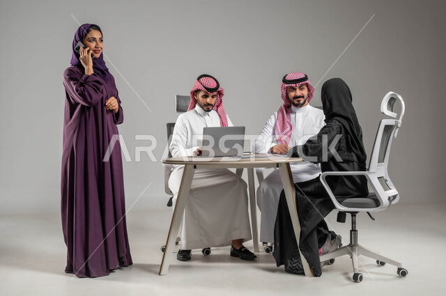إجراء مكالمات عمل، الاحترافية والتفاني في العمل، إستخدام التكنولوجيا الحديثة ، بورتريه لموظفين عرب سعوديين خليجيين في اجتماع، مهن ووظائف سعودية، مفهوم الشراكة والتعاون، الحوارات والنقاشات ضمن الفريق، توفير بيئة عمل مناسبة، صورة لكامل الجسم، خلفية رمادية