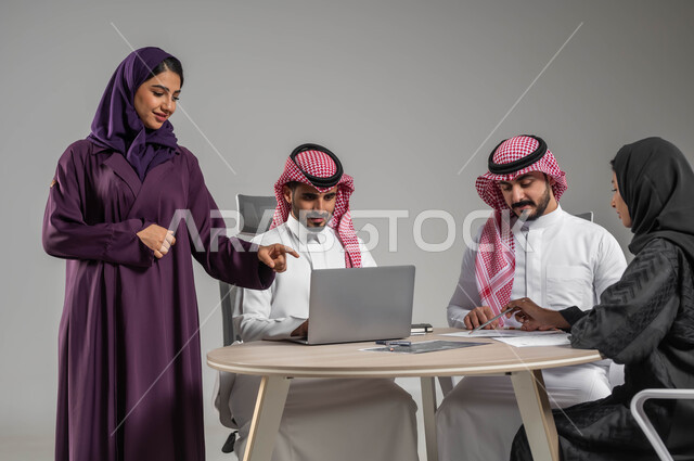الإشارة إلى اللابتوب بهدف توضيح العمليات و الإجرائات، إستخدام جهاز الحاسوب المحمول ، بورتريه لموظفين عرب سعوديين خليجيين في اجتماع، مهن ووظائف سعودية، مفهوم الشراكة والتعاون، الحوارات والنقاشات ضمن الفريق، توفير بيئة عمل مناسبة، خلفية رمادية
