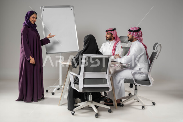 شرح مهام الأعمال، التعاون وروح الفريق، استخدام السبورة لتوضيح العمليات والاجراءات المتبعة في الشركة، الاشارة إلى اللوح بهدف التوضيح، مناقشة خطط العمل، ضمان فهم واضح للاعمال، الاحترافية والتفاني في الإنجاز، بورتريه لفريق عربي خليجي سعودي في اجتماع، خلفية رمادية