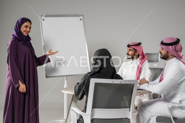 العمل الجماعي وروح الفريق، مناقشة خطط العمل، ضمان فهم واضح للاعمال، استعمال السبورة لتوضيح العمليات والاجراءات المتبعة في الشركة، استخدام اللابتوب في تدوين الملاحظات، الاحترافية في الإنجاز، بورتريه لفريق عربي خليجي سعودي في اجتماع، صورة لكامل الجسم، خلفية رمادية