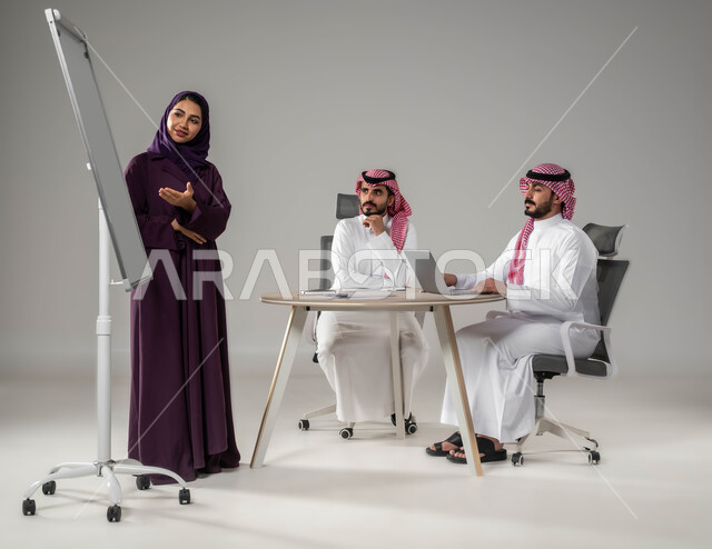مناقشة خطط العمل، شرح مهام الاعمال، ضمان فهم واضح للاعمال، استخدام السبورة لتوضيح العمليات والاجراءات المتبعة في الشركة، استعمال اللابتوب في تدوين الملاحظات، الاحترافية والتفاني في الإنجاز، بورتريه لفريق عربي خليجي سعودي في اجتماع، صورة لكامل الجسم، خلفية رمادية