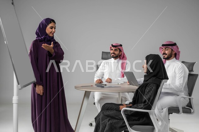 الاشارة إلى اللوح بهدف التوضيح، مناقشة خطط العمل، ضمان فهم واضح للاعمال، استخدام السبورة لتوضيح العمليات والاجراءات المتبعة في الشركة، استعمال اللابتوب في تدوين الملاحظات، الاحترافية والتفاني في الإنجاز، بورتريه لفريق عربي خليجي سعودي في اجتماع، خلفية رمادية