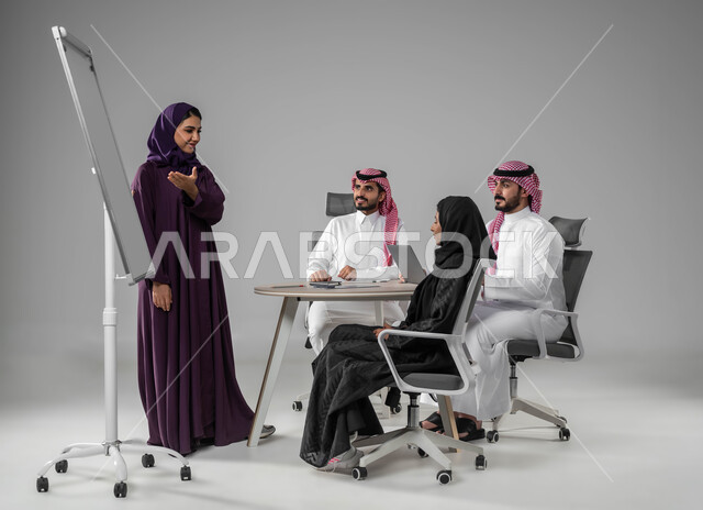 استعمال اللابتوب في تدوين الملاحظات، ضمان فهم واضح وشامل للاعمال، استخدام السبورة لتوضيح العمليات والاجراءات المتبعة في الشركة، الاحترافية في الإنجاز، شرح مهام الاعمال، بورتريه لفريق عربي خليجي سعودي في اجتماع، مناقشة خطط العمل، صورة لكامل الجسم، خلفية رمادية