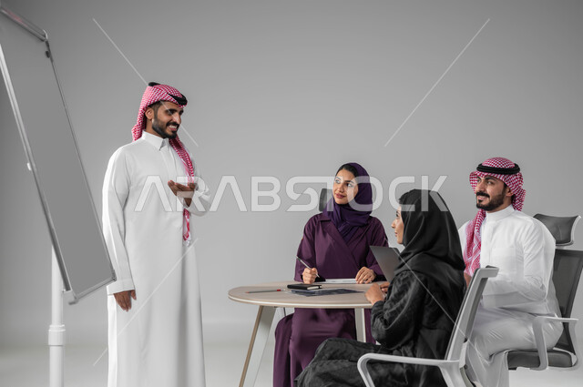 روح الفريق والعمل الجماعي، مناقشة خطط العمل، ضمان فهم واضح وشامل للاعمال، استعمال السبورة لتوضيح العمليات والاجراءات المتبعة في الشركة، استخدام اللابتوب في تدوين الملاحظات، الاحترافية والتفاني في الإنجاز، بورتريه لفريق عربي خليجي سعودي في اجتماع، خلفية رمادية