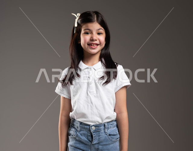 ايماءات تدل على السعادة، التقاط صور شخصية للوثائق المدرسية, الإهتمام بالمظهر الخارجي للأطفال الصغار، بورتريه مقرب لطفلة عربيه خليجيه سعودية تنظر إلى الكاميرا مبتسمة ترتدي زي كاجوا، ارتداء الملابس الجديده في الأعياد والمناسبات، خلفيه رمادية