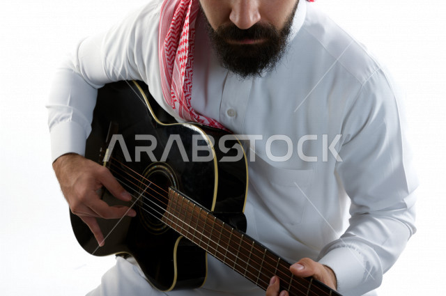 بورتريه شاب سعودي عربي خليجي يعزف على  الجيتار( آلة وترية) ، شاب باللباس السعودية التقليديه بخلفية بيضاء ، آلة موسيقية ، مجال صوتي و فني