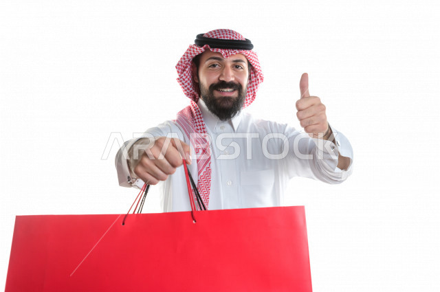 Portrait of a Saudi Gulf man carrying shopping bags, buying gifts, entertainment and shopping, on a white background
