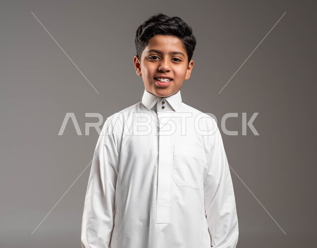 التقاط صورة شخصية للوثائق الرسمية، بورتريه مقرب لولد عربي خليجي سعودي مبتسم يرتدي الثوب التقليدي وينظر الى الكاميرا بتعابير السرور، الوقوف باستقامة وثقة بالنفس، مفهوم الاهتمام بالمظهر الخارجي, خلفية رمادية