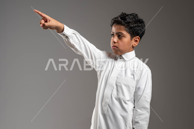 تعابير وايماءات تدل على اليأس وعدم الرضا، مفهوم رؤية الأشياء البعيدة، بورتريه مقرب لفتى عربي خليجي سعودي يرتدي الزي التقليدي يرفع يده الى الأعلى ويشير الى مكان ما بتعابير الحزن، حركات تدل على تحديد موقع معين، خلفية رمادية