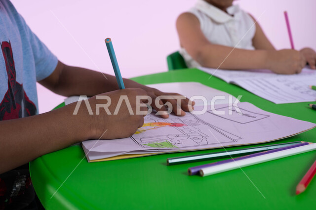 Skills and activities that help develop mental and intellectual abilities, art classes and sessions in Saudi kindergartens, a close-up portrait of Saudi Gulf Arab children wearing casual clothes, actively creating drawings and coloring, a pink background.