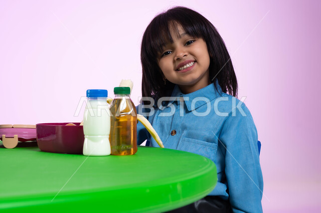 تعليم الأطفال أسس الغذاء الصحي السليم، بورتريه مقرب لطفلة عربية خليجية سعودية ترتدي الزي الكاجوال تنظر إلى الكاميرا تتناول الأطعمة الصحية في وقت الفسحة المدرسية في إحدى المدارس السعودية