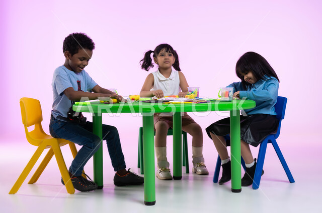 قضاء أوقات ممتعة ومفيدة في الروضة, تنمية الجانب الحركي والابتكاري لدى الأطفال، تعلم صنع أشكال ومجسمات باستخدام العجينة الملونة, النشاطات الفنية والحركية, بورتريه لأطفال عرب خليجيين سعوديين يبدعون بنشاط اللعب بالمعجون الملون، خلفية وردية