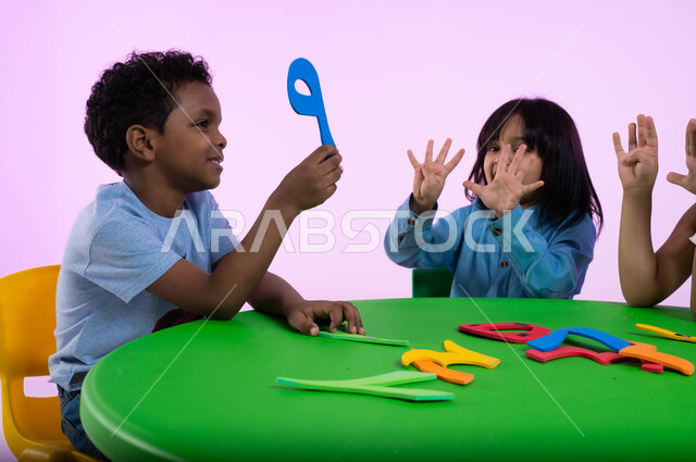 القيام بالعمليات الحسابية في مادة الرياضيات، بورتريه لأطفال عرب خليجيين سعوديين يرتدون الزي الكاجوال يقومون بالدراسة عن طريق الألعاب، ايماءات الحماس والسرور، تنمية القدرات الفكرية ومهارات الحساب لطلاب المرحلة التمهيدية,  جودة التعليم في السعودية، خلفية وردية