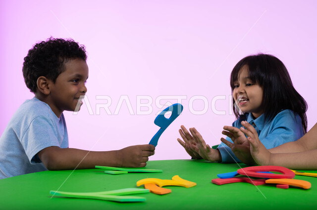 التعاون والمشاركة بين أطفال الروضة في تعلم الرياضيات، تعلم الأرقام والأعداد العربية وأشكالها،  بوتريه لأطفال عرب خليجيين سعوديين يرتدون الزي الكاجوال يتعلمون الحساب، نشاطات ترفيهية وتعليمية تساعد على تنمية القدرات الفكرية، خلفية وردية.