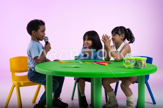 تنمية مواهب الأطفال في الروضة, موهبة الغناء والتدريب الصوتي، إيماءات الإندماج والتفاعل مع الموسيقا، بورتريه لأطفال عرب خليجيين سعوديين يرتدون الزي الكاجوال يستمتعون بالغناء والتصفيق، تقديم العروض الفنيه المسرحيه الغنائيه، تسجيل مقطع صوتي غنائي، خلفيه وردية