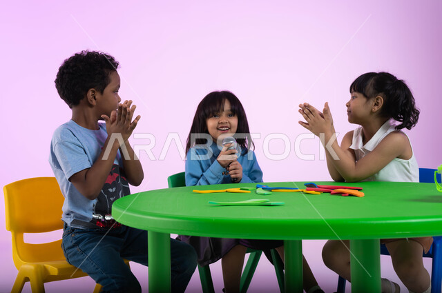 Singing talent and vocal training, gestures of integration and interaction with music, a portrait of Saudi Gulf Arab children wearing casual clothes enjoying singing and clapping, presenting musical theatrical performances, recording a singing audio clip, developing children’s talents in kindergarten, pink background