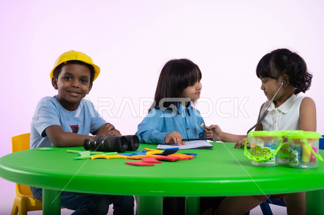 شرح وتعليم المهن والوظائف المستقبلية للأطفال، الشغف بمهنة الهندسة منذ الطفولة، بورتريه لأطفال عرب خليجيين سعوديين يرتدون الزي الكاجوال يتعرفون في الروضة عن مفهوم الطب والرعاية الصحية، طفلة سعودية تقوم بالفحص بواسطة السماعة الطبية، خلفية وردية.