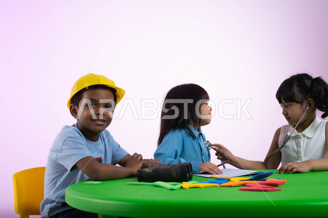 اختيار وتحديد المهنة المستقبلية منذ الصغر، الشغف بمهنة الهندسة منذ الطفولة،  بورتريه لأطفال عرب خليجيين سعوديين يرتدون الزي الكاجوال يتعلمون في الروضة مفهوم الطب والرعاية الصحية،طفلة سعودية تقوم بالفحص بواسطة السماعة الطبية، خلفية وردية.