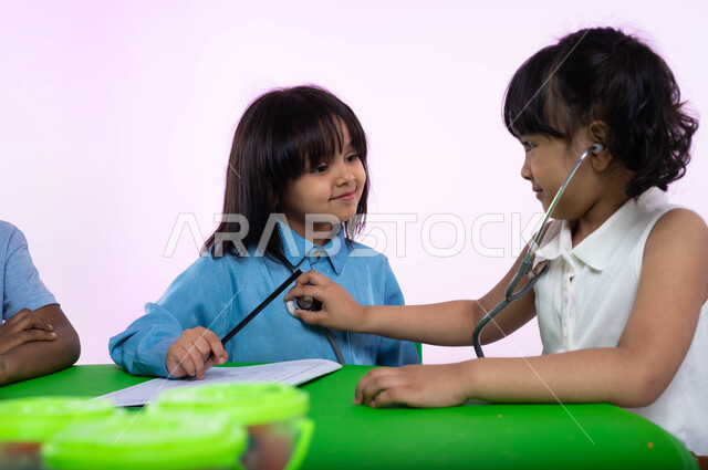 تعريف الأطفال في الروضة مفهوم الطب والرعاية الصحية، بورتريه لأطفال عرب خليجيين سعوديين يرتدون الزي الكاجوال يقومون بالفحص بواسطة السماعات الطبية، اختيار وتحديد المهنة المستقبلية منذ الصغر، الشغف بمهنة الطب منذ الطفولة، خلفية بيضاء.