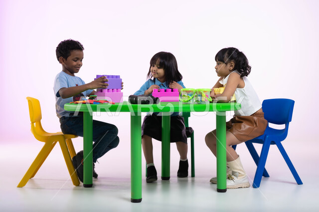 مهارات وأنشطة تساعد على التطور الفكري، الجلسات والحصص الإبداعية في الروضات السعودية،  إيماءات وجه تدل على السعادة والمتعة والتركيز، بورتريه لأطفال عرب سعوديين خليجيين يرتدون الزي الكاجوال يستمتعون بتركيب المكعبات، خلفية وردية.