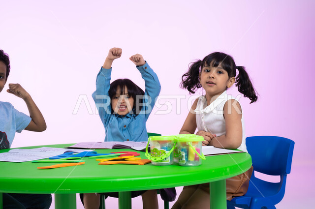 المنافسة والتحدي والتشجيع في النشاطات بين الأطفال في الروضة، بورتريه مقرب لأطفال عرب خليجيين سعوديين يرتدون الزي الكاجوال يرفعون أيديهم، إيماءات يدين تدل على الحماس والشغف، الفرح والسعادة بالفوز والانتصار، خلفية وردية.