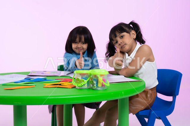 النظر إلى الكاميرا بإيماءات الجودة والامتياز, بورتريه لأطفال روضة عرب خليجين سعوديين يرتدون الزي الكاجوال يتعلمون في إحدى الروضات السعودية, المشاركة والتعاون في الحصص التعليمية, خلفية ملونة