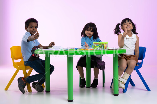 طرق تعليم ترفيهية للأطفال في المملكة العربية السعودية، النظر إلى الكاميرا، إيماءات وجه ويدين تدل على الرضا والقبول والإعجاب، بورتريه لأطفال عرب خليجيين سعوديين يرتدون الزي الكاجوال يشيرون بإصبعهم الإبهامي علامة لايك، خلفية ملونة.