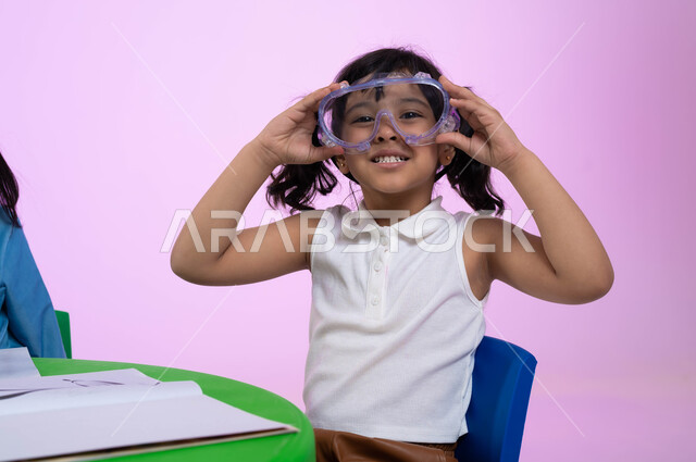 اللعب واللهو بأدوات المسبح، أنشطة ترفيهية وتعليمية للأطفال، بورتريه مقرب لطفلة عربية خليجية سعودية ترتدي الزي الكاجوال ونظارات السباحة بإيماءت السعادة والسرور، الحماس والشوق للغوص في الماء، الاستعداد والتحضير للسباحه في الروضات السعودية، خلفية وردية