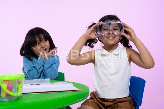 الاستعداد والتحضير للسباحه في الروضات السعودي، اللعب واللهو بأدوات المسبح، أنشطة ترفيهية وتعليمية للأطفال، بورتريه مقرب لطفلة عربية خليجية سعودية ترتدي الزي الكاجوال ونظارات السباحة بإيماءت السعادة والسرور، الحماس والشوق للغوص في الماء، خلفية وردية